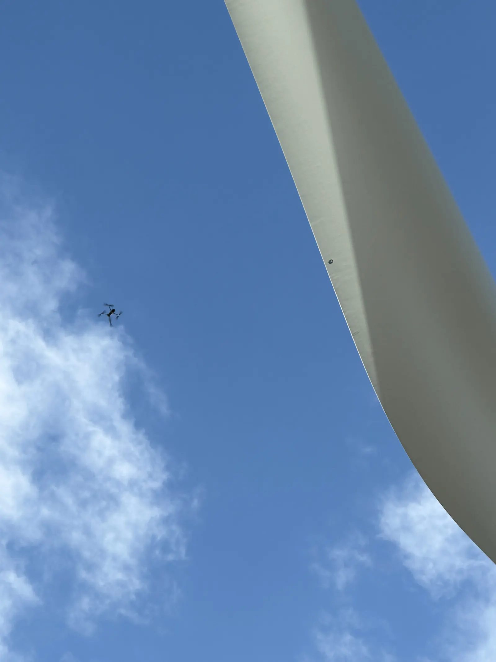 Inspection drone flying beside a wind turbine blade in a blue sky