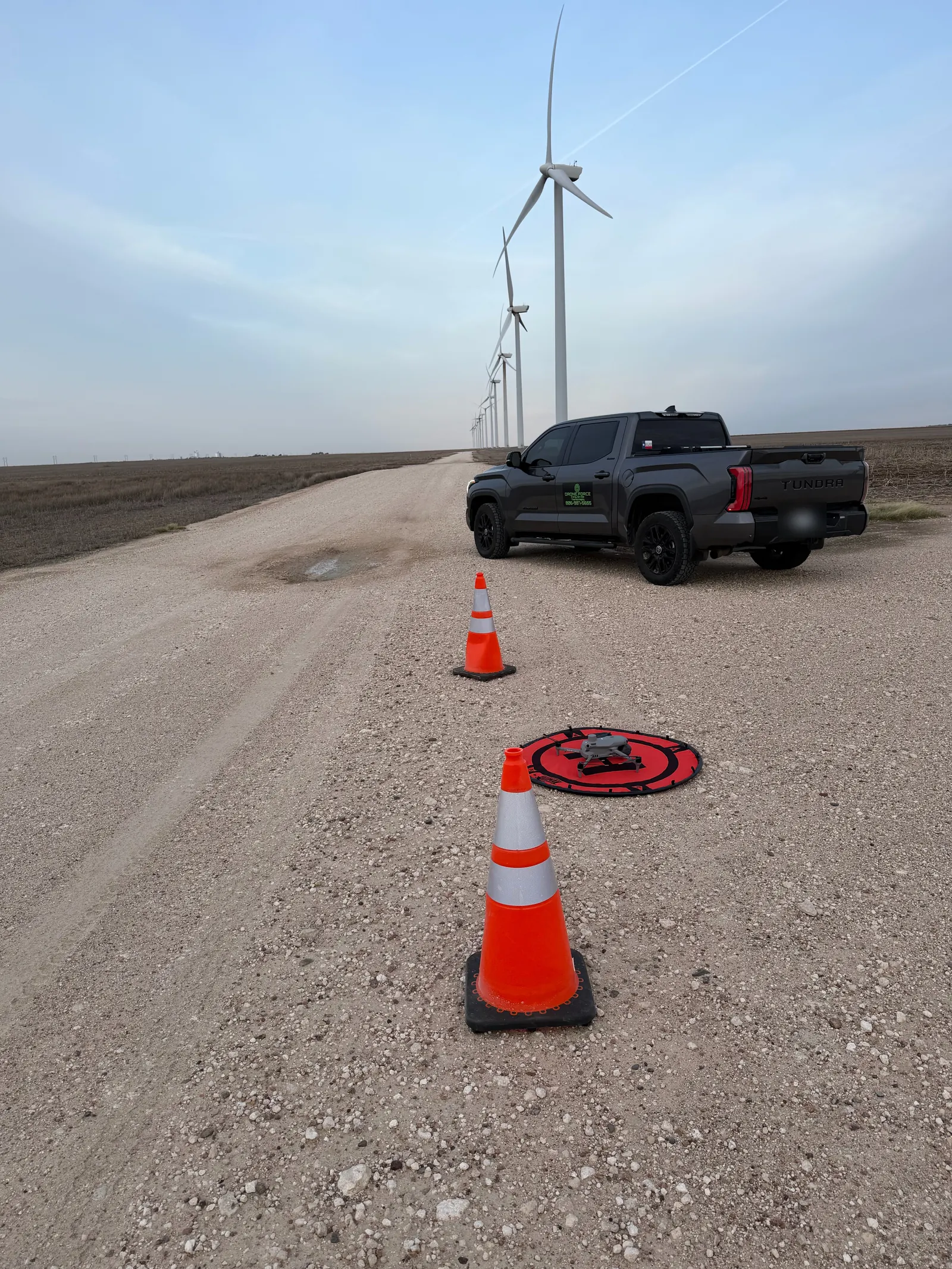 Drone Force truck with safety cones and the drone on a red landing pad, turbine row behind