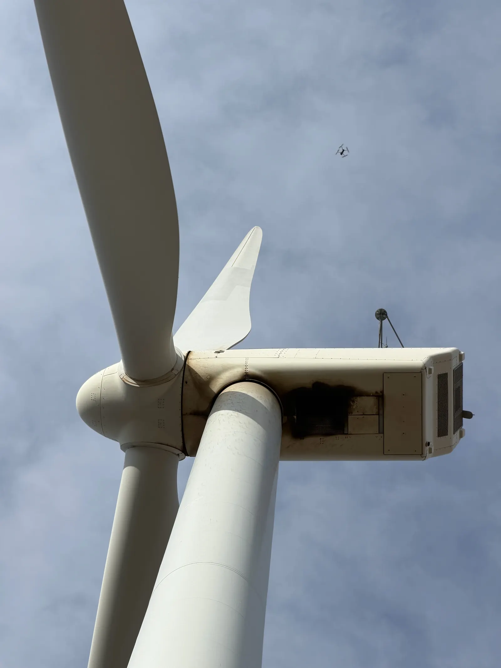 Inspection drone flying near a wind turbine nacelle on a cloudy day
